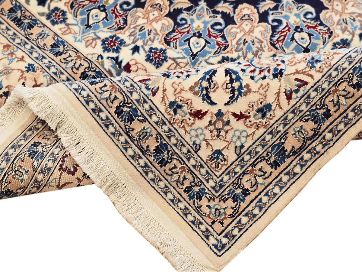Corner detail of Nain rug showing fringed edge and navy floral border patterns.