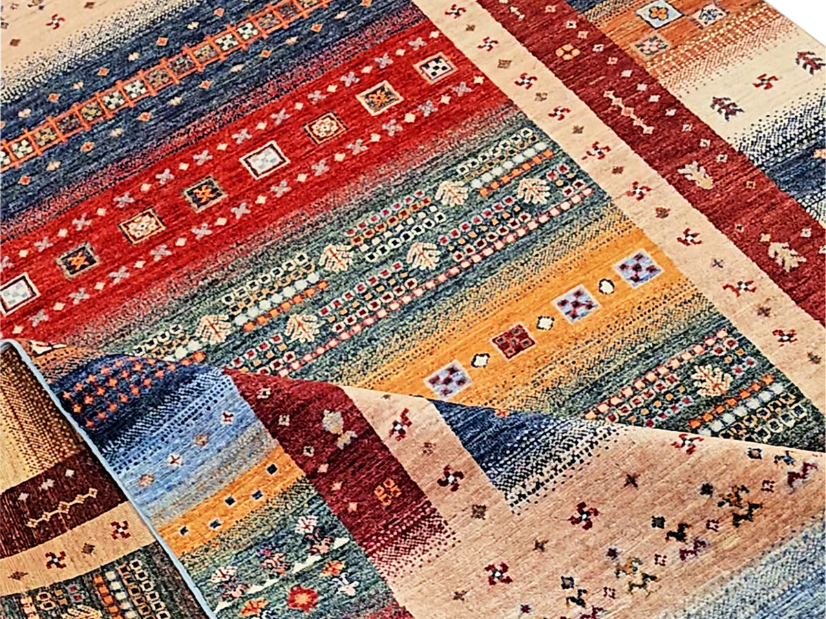 Close-up rug showing layered geometric bands in red, blue, and beige with fringe.