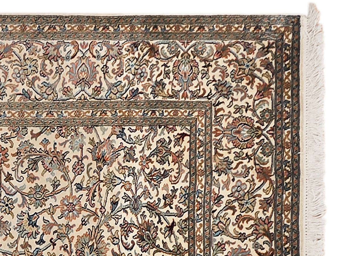Beige silk rug corner with floral vines, dark border, and fringed edge