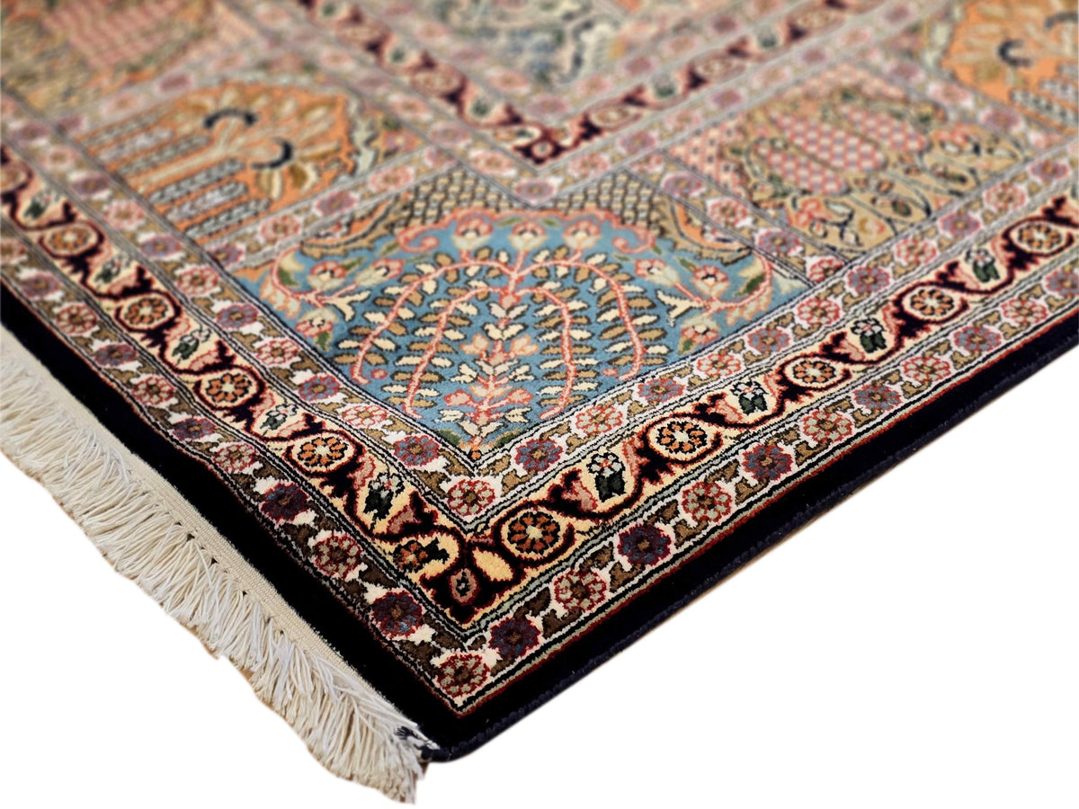 Corner view of multicolor ornate rug with blue field, dark border, and fringe.