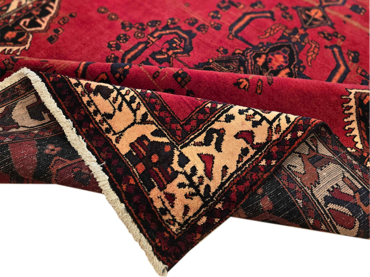 Red patterned rug with cream fringe edge and detailed central shapes in black and beige