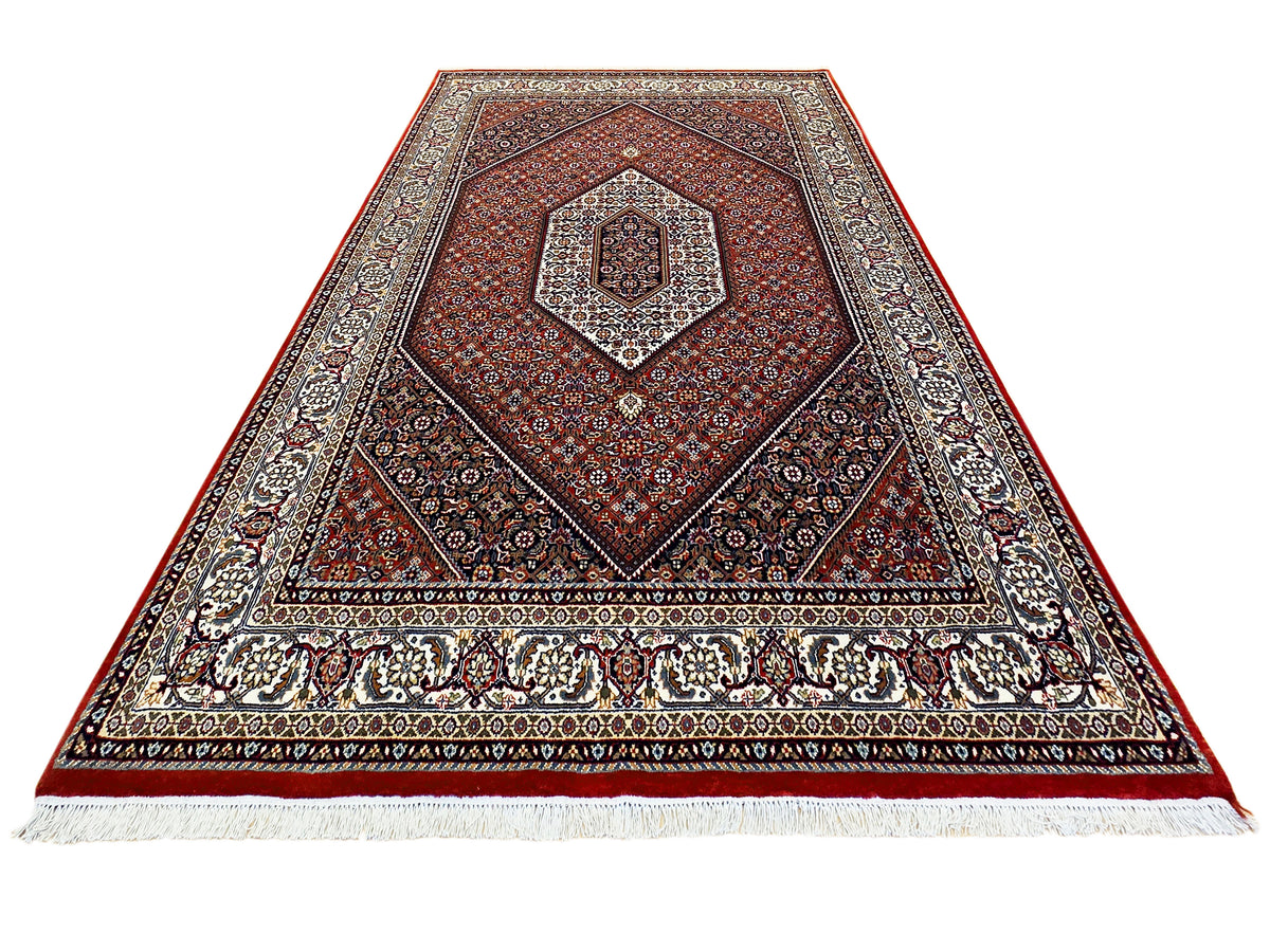 Rectangular area rug in red and dark tones with central diamond medallion and cream fringe