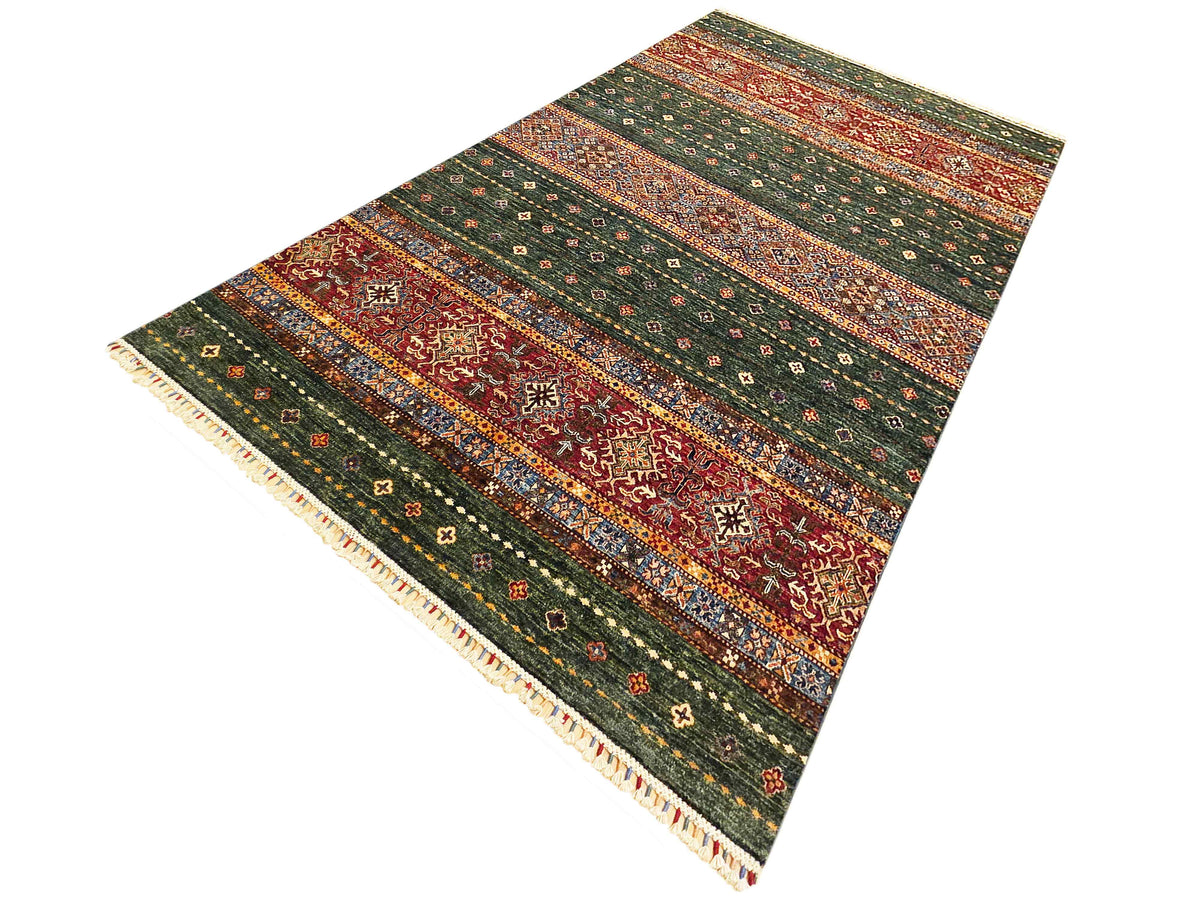 Green, red, and orange patterned rectangular rug with cream fringe along edges