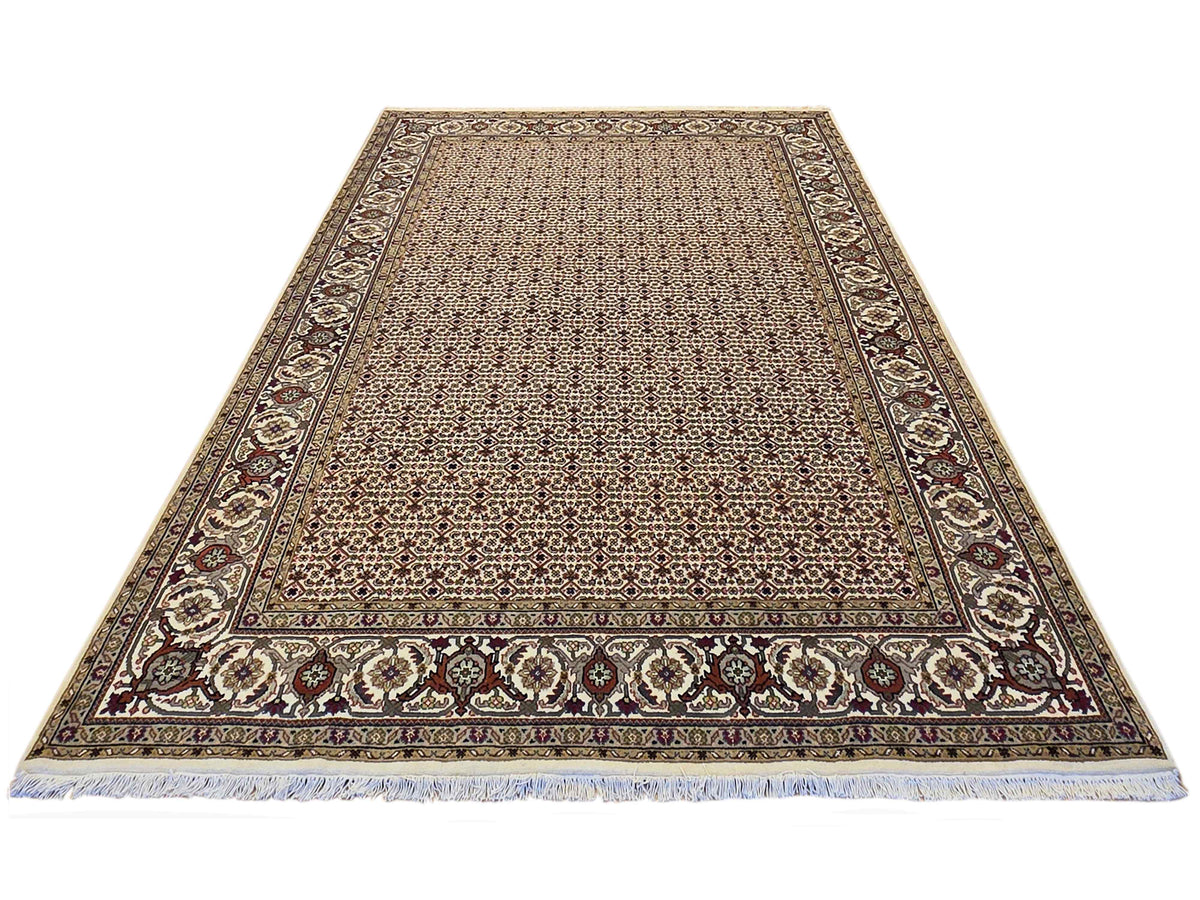 Beige area rug with dark patterned field, floral corner panels, and light blue fringe