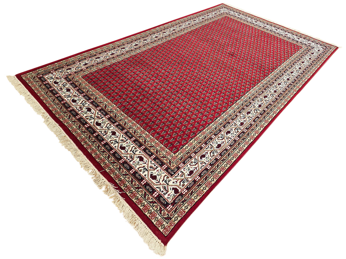 Red medallion-style area rug with multi-line ornamental border and cream fringed corners