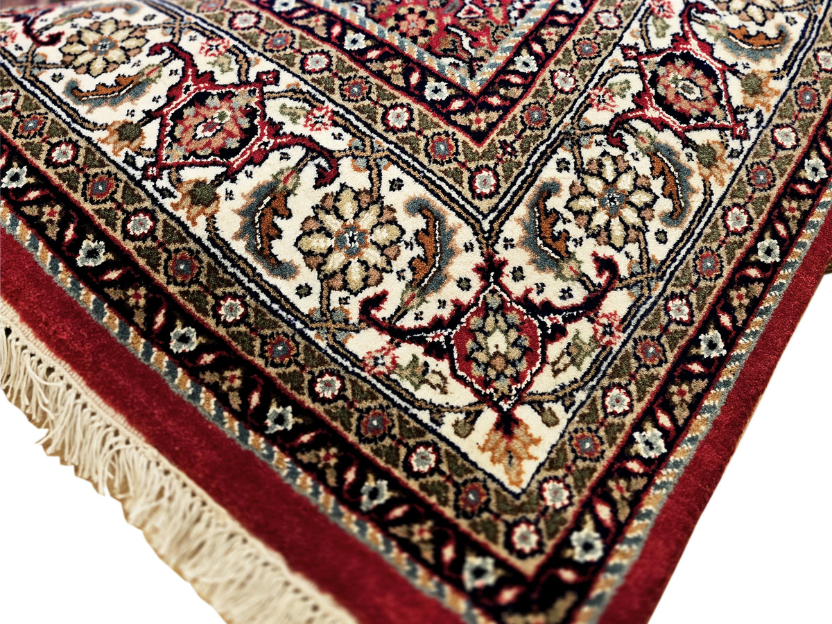 Close-up of red rug field with cream and black floral motifs and short fringe