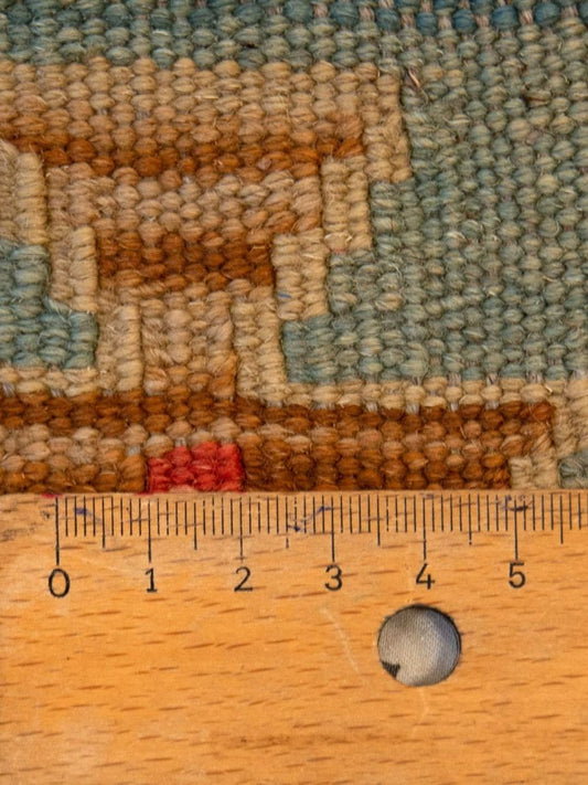 Close-up of multicolor kilim rug texture with geometric border; includes measuring tape