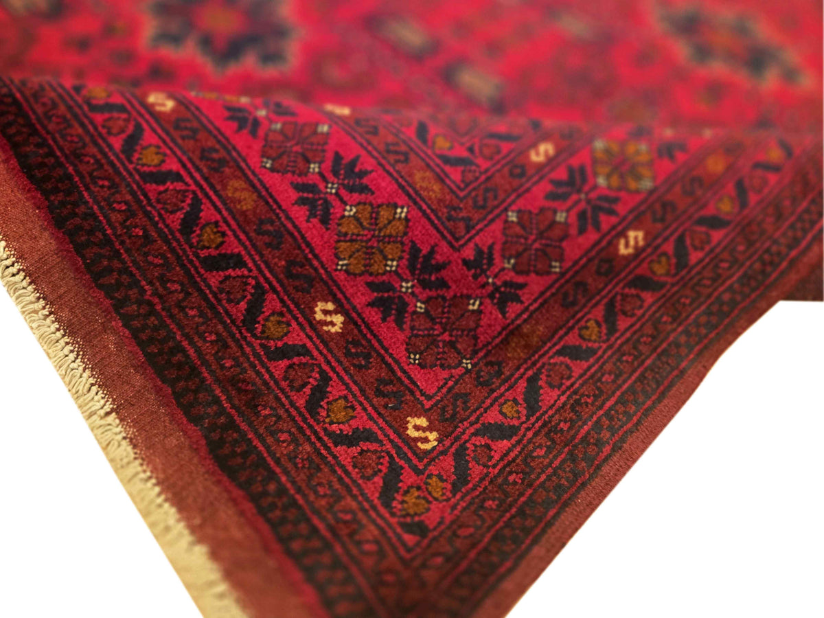 Red patterned area rug corner with zigzag border and light fringe trim