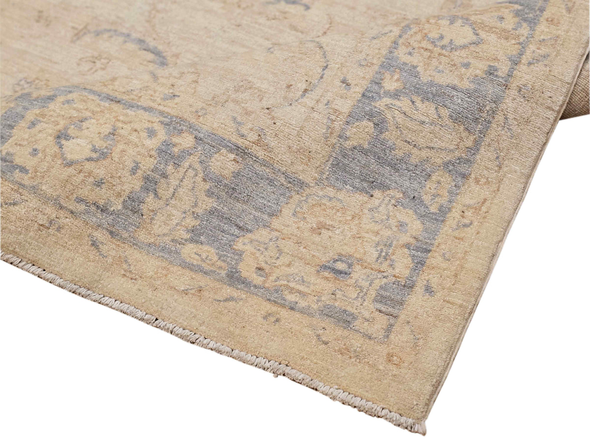 Corner of beige area rug with light blue geometric motifs and short fringe edging
