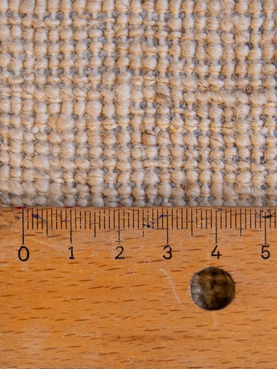 Close-up woven rug texture in beige and dark flecks, with ruler for scale
