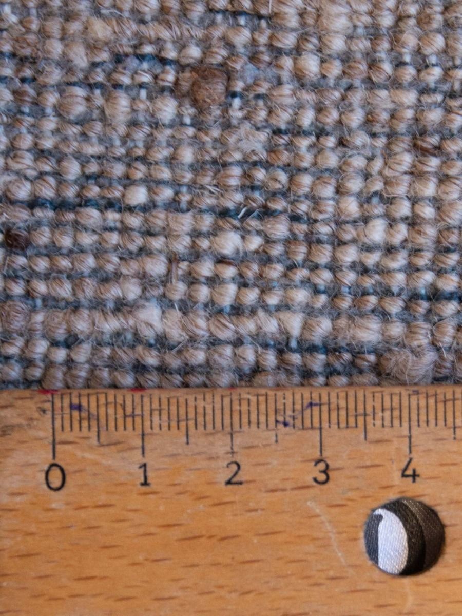 Woven rug texture close-up in blue and tan with tape measure along the pile