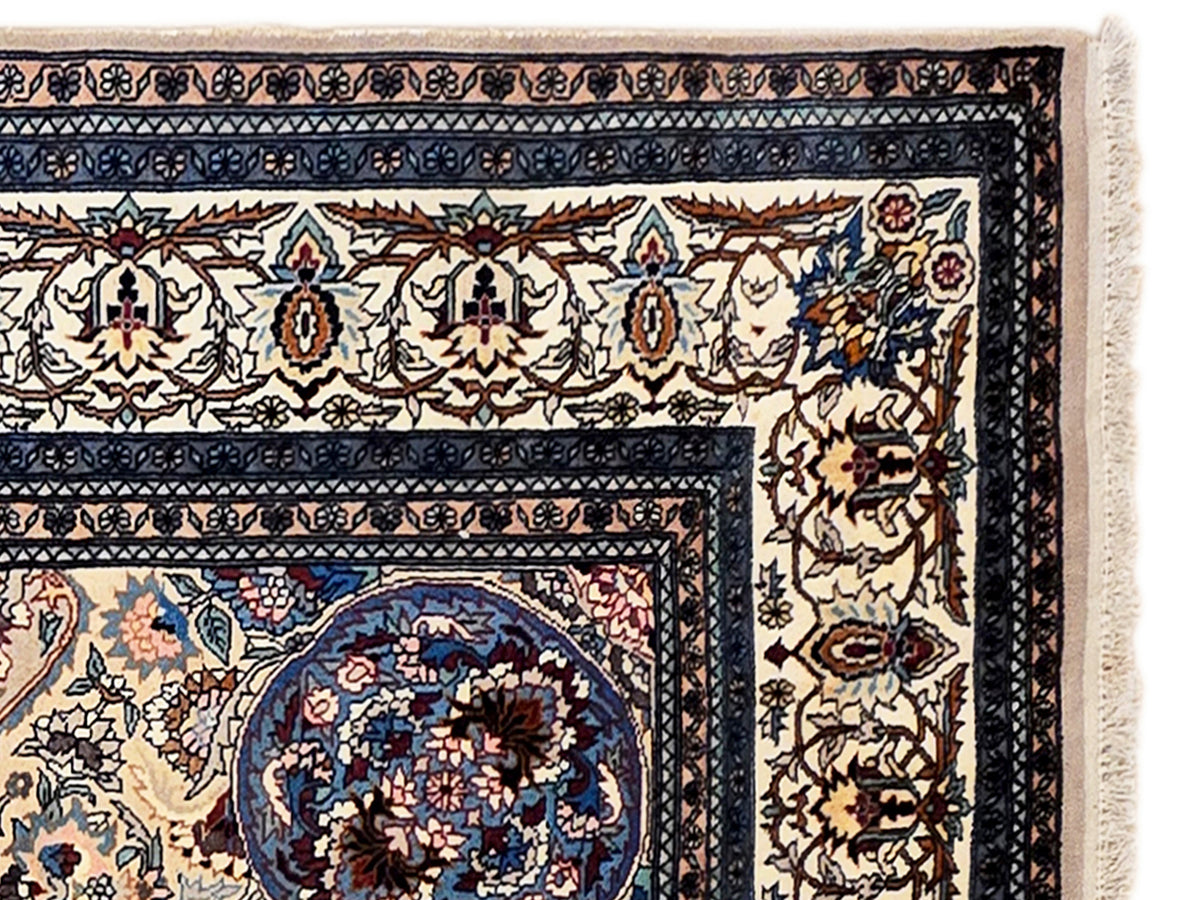 Close-up of blue patterned Tabriz-style rug border and corner motifs with beige fringe.