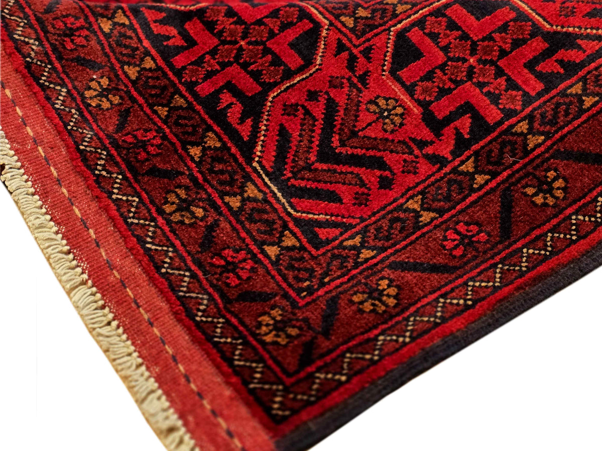 Corner view of red rug with bold geometric pattern and stitched edge with fringe.