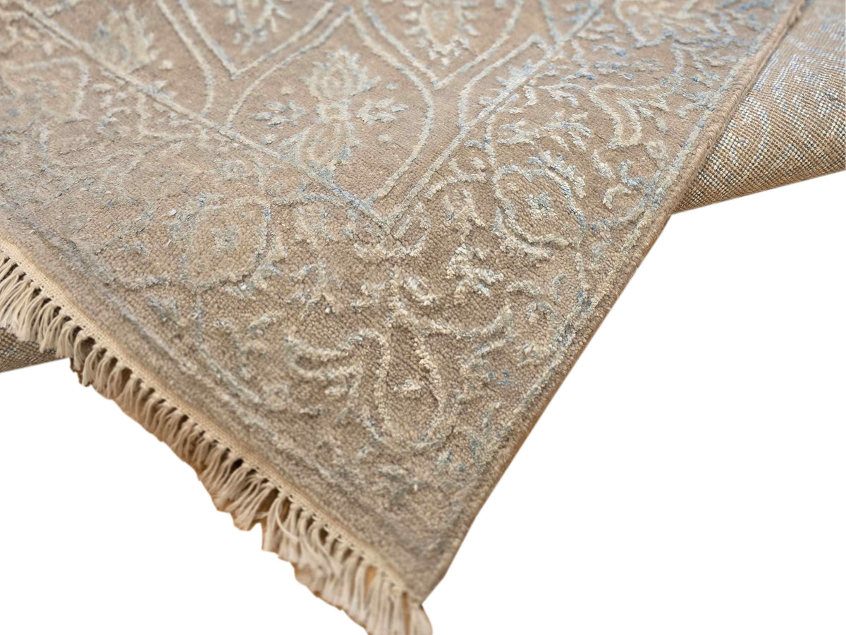 Corner detail of light blue-gray rug with ornate pattern and tasseled fringe.