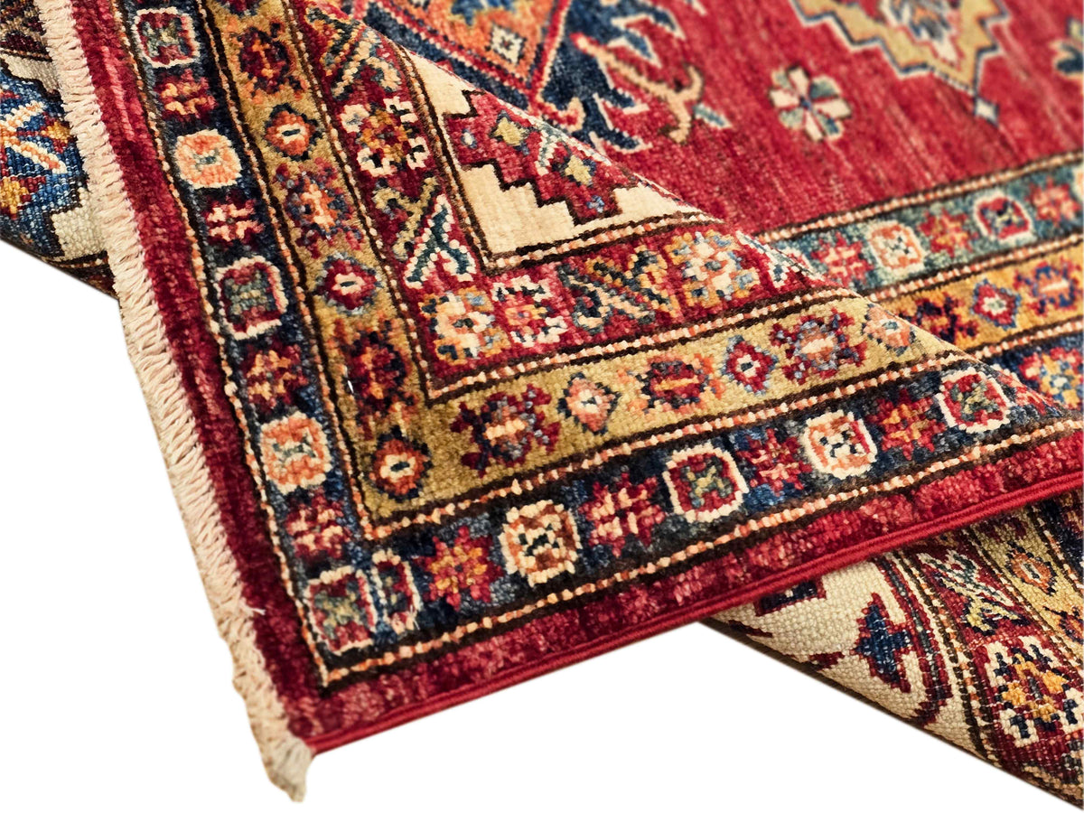 Close-up of rug corner with red ground, cream shapes, and blue geometric bands
