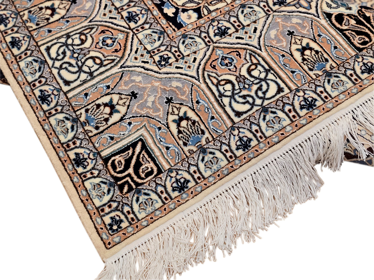 Close-up of beige and blue rug corner with fringed edge and ornate geometric motifs.