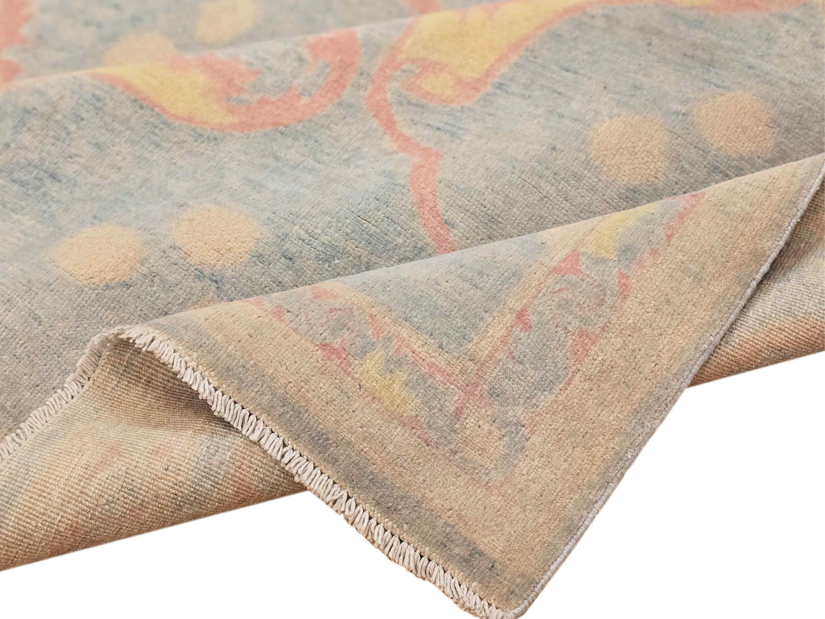 Rug corner detail: light blue-gray field with coral pattern and stitched fringe edge