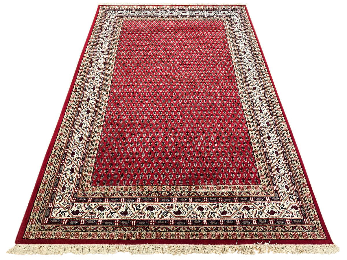 Red patterned area rug with ornate cream, black, and gold border and cream fringes