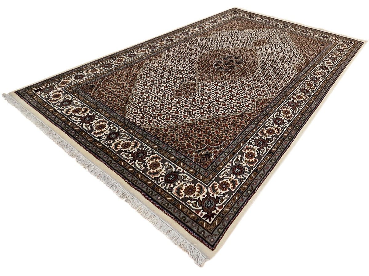 Diagonal view oriental rug with brown medallion, cream micro-pattern, dark navy border, fringe