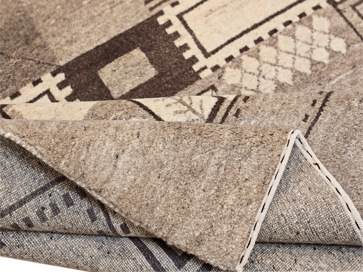 Folded edge of geometric patchwork rug in beige and gray with stitched pattern