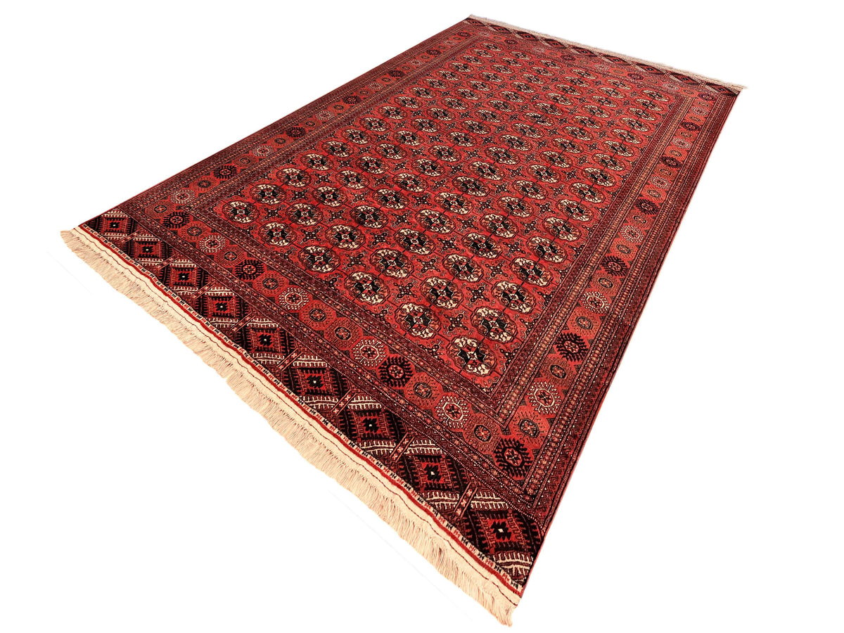 Red rug laid flat with repeating medallions, dark accents, and cream fringes