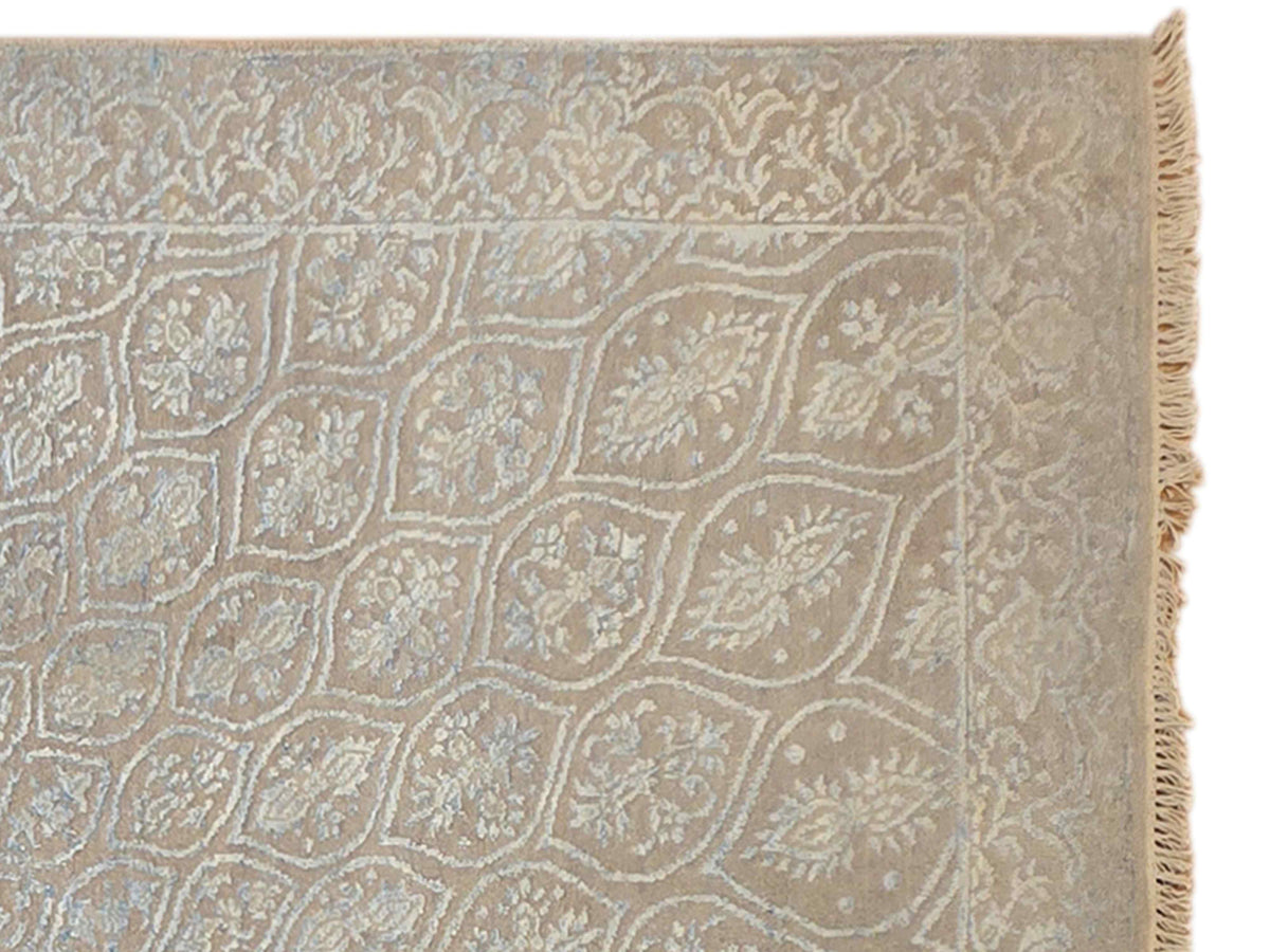 Close-up of light blue-gray rug corner showing ornate pattern and short fringe.