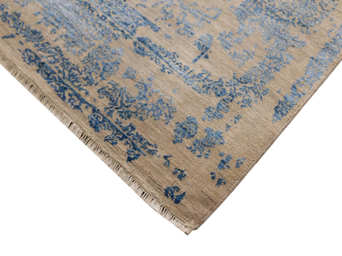 Corner detail of beige rug with blue distressed medallion pattern and short fringed trim.