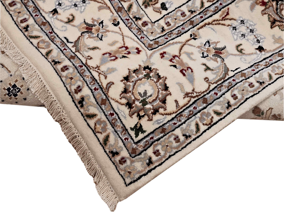Close-up corner of cream rug with floral vines, blue trim lines, and short fringe