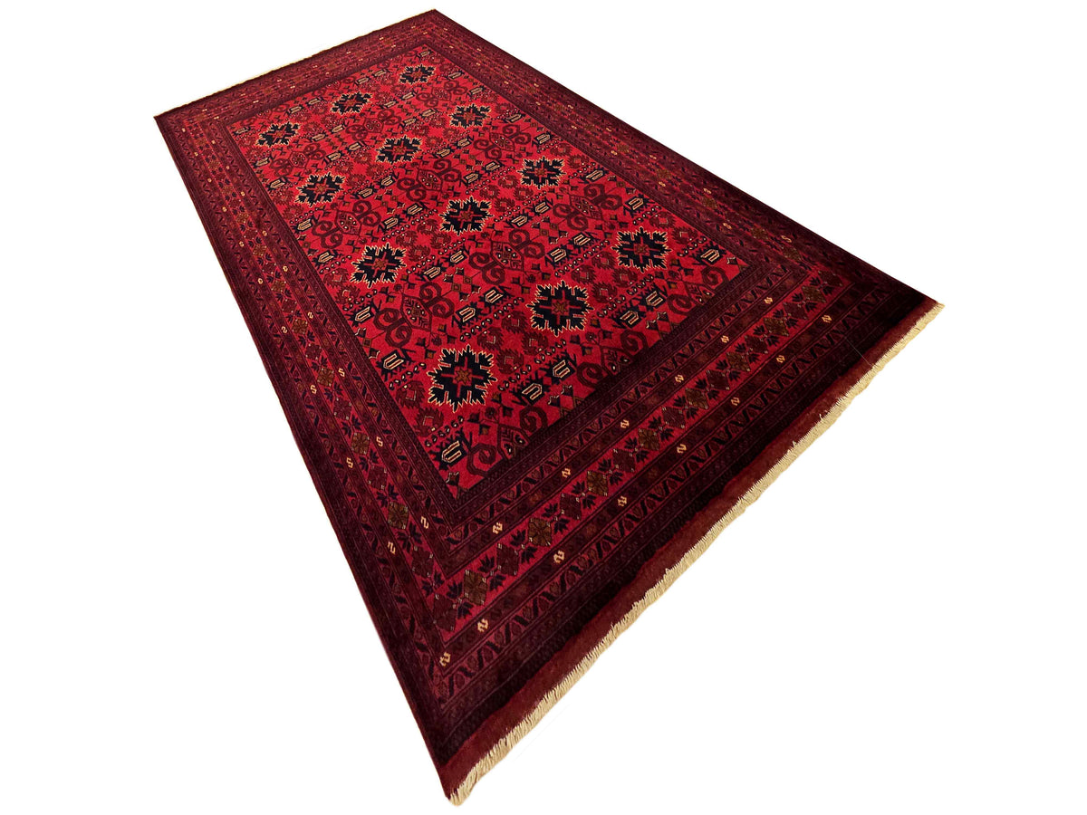 Red patterned area rug shown at an angle with border details and fringe