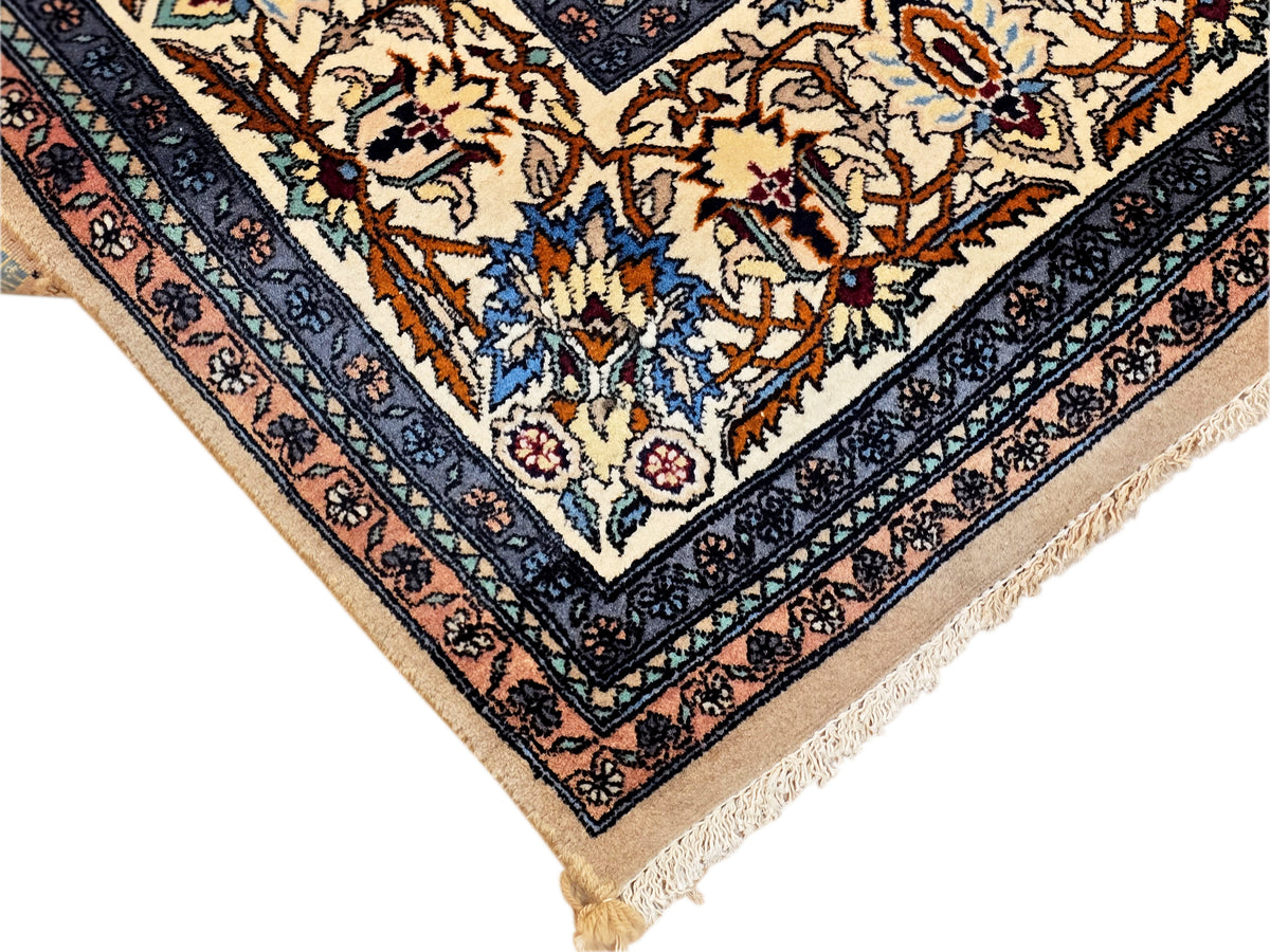 Corner detail of blue Tabriz-style rug with floral vines, orange accents, and beige fringe.