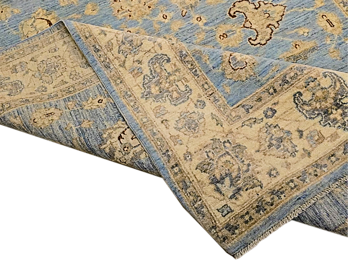 Rolled edge view of light blue and beige ornate area rug with border trim