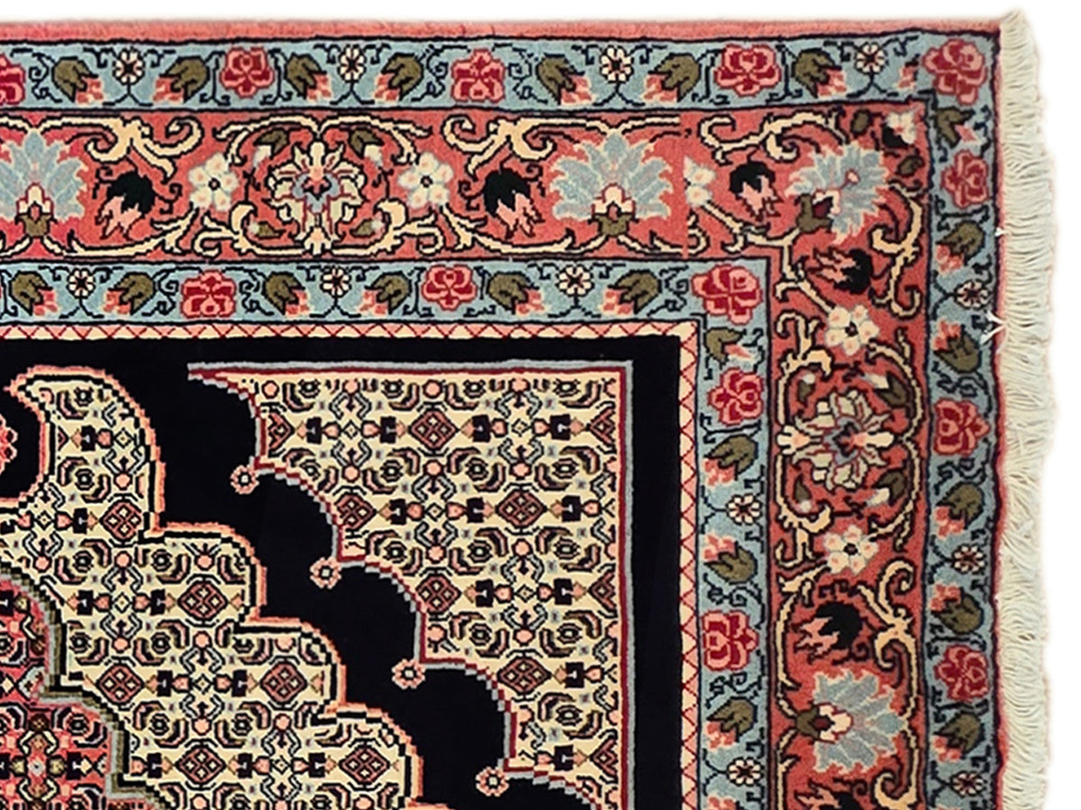 Decorative patterned area rug with red, navy, and cream motifs and fringed edge.