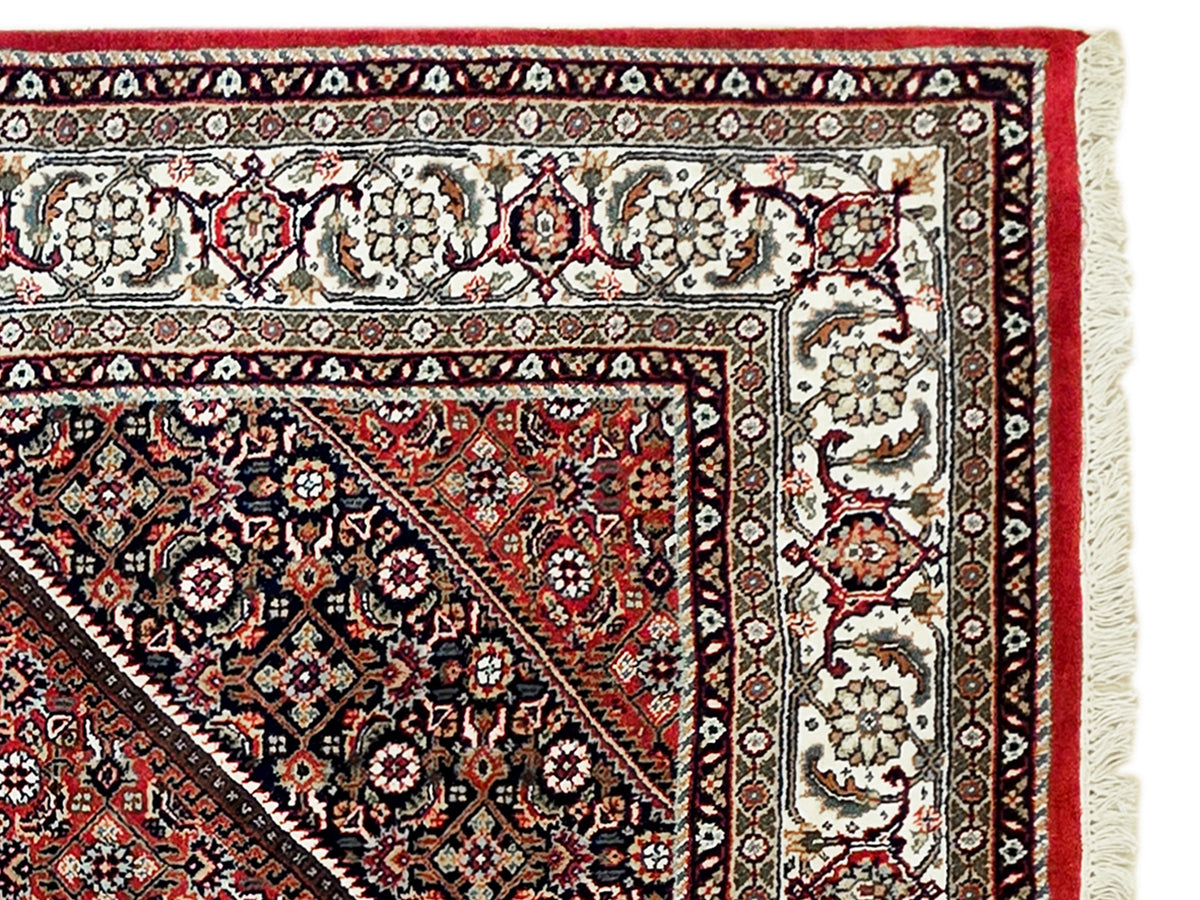 Close-up of red and black rug border with ornate floral motifs and cream edge