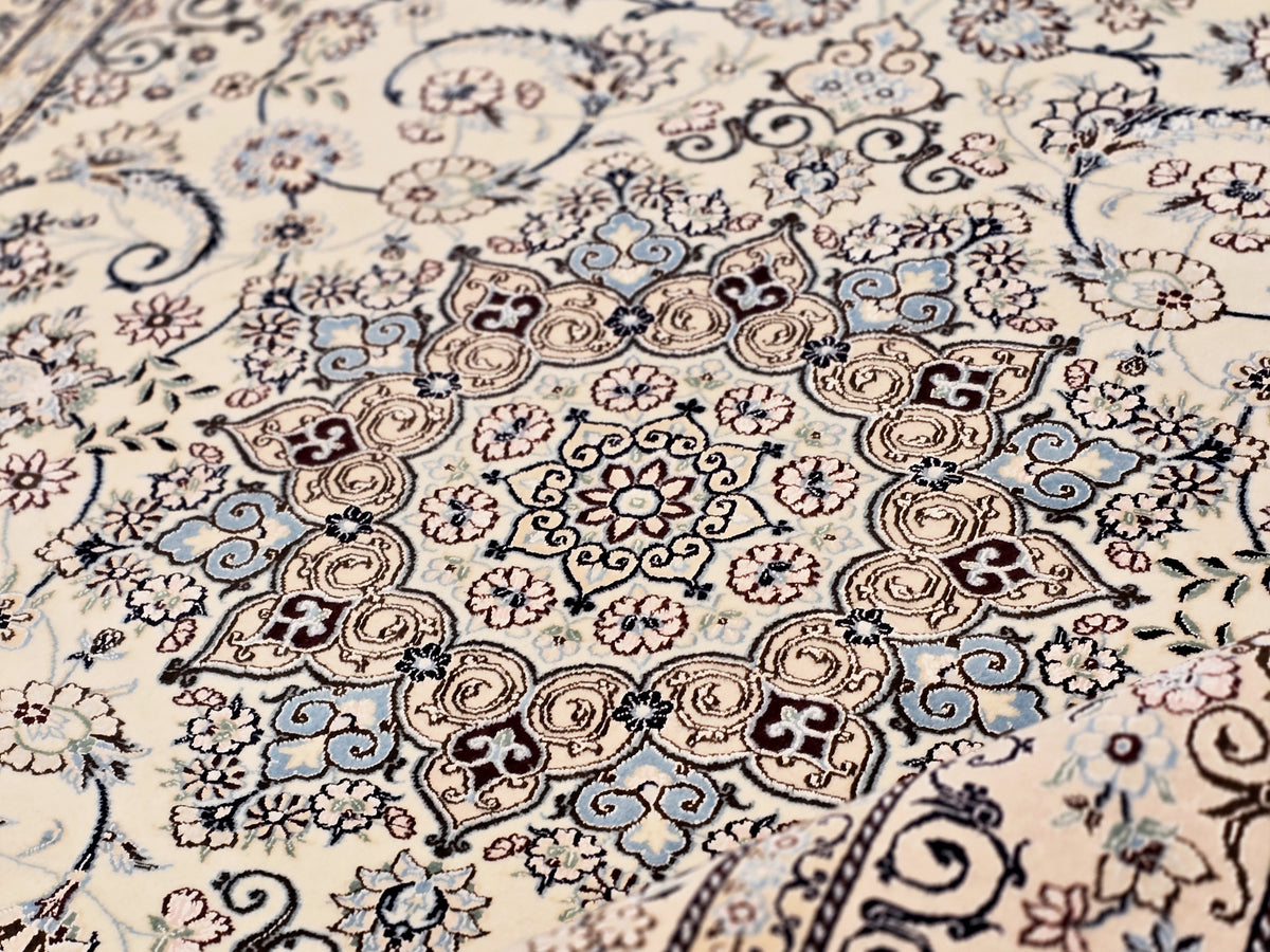 Close-up of cream area rug with blue and tan swirls, flowers and ornate border