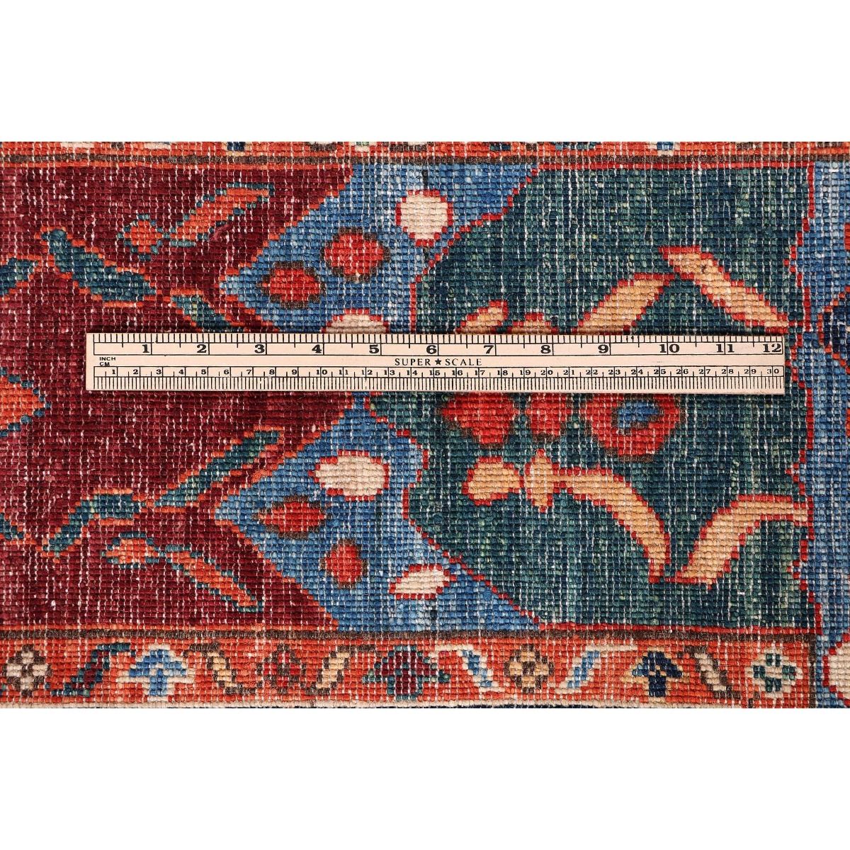 Rug measuring detail with dense red and blue motifs on cream highlights; scale tape visible.